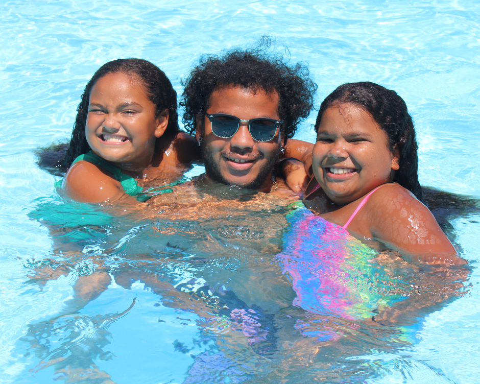 A young boy and two young girls posing with their arms around each other's shoulders in the pool at Camp Cann-Edi-On