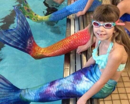 Young girl in a mermaid tail smiling by the side of YWCA York's pool